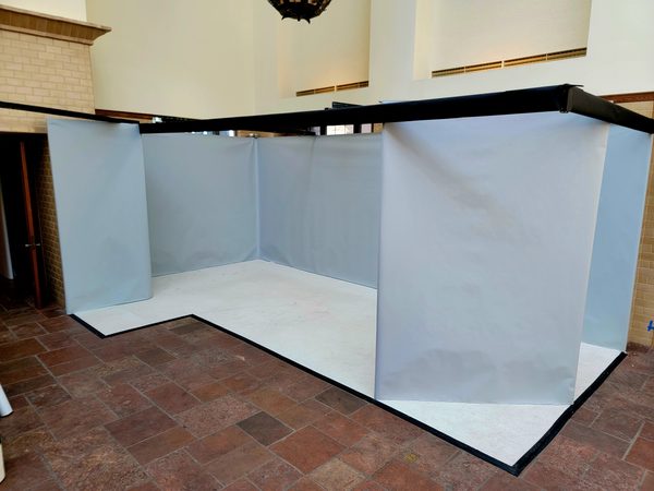 L-shaped booth with light gray walls, black framing and white floor covering on a reddish tile floor, Omaha 2023